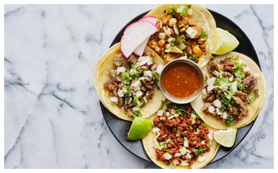 A variety of street tacos with salsa and limes.